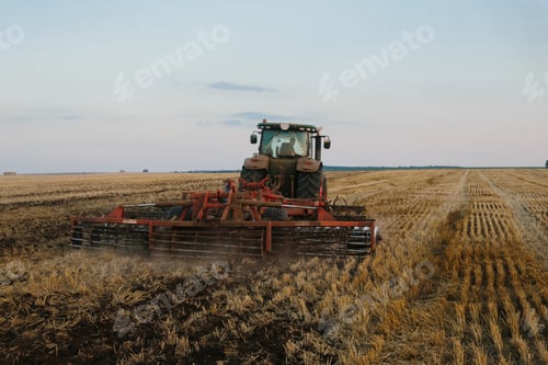 Preview: Modern tractor with a heavy trailed disc harrow works a wide hilly field.