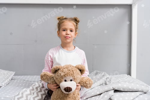Preview: adorable little kid with teddy bear sitting on bed