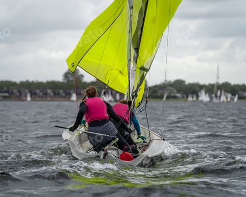 Preview: Two women sailing on a small boat with bright yellow sails on a cloudy day