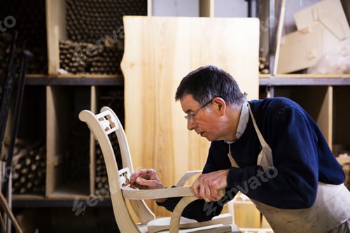 Preview: Man standing in a carpentry workshop, working on a wooden chair marking the armrest joint with a