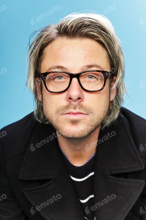 Preview: Studio Portrait Of Young Man With Long Blond Hair Wearing Glasses And Black Jacket. Isolated On