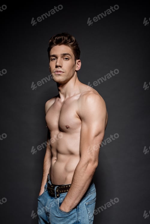 Preview: sexy young man with muscular torso posing with hands in pockets on black background