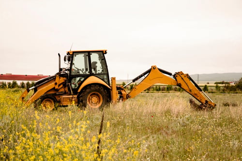 Preview: Tractor excavator against the background of spring flowers in the field. Preparing fields for sowing
