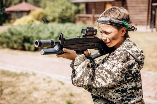 Preview: Teenager boy with weapon in his hand playing laser tag shooting game in outdoor. War simulation game