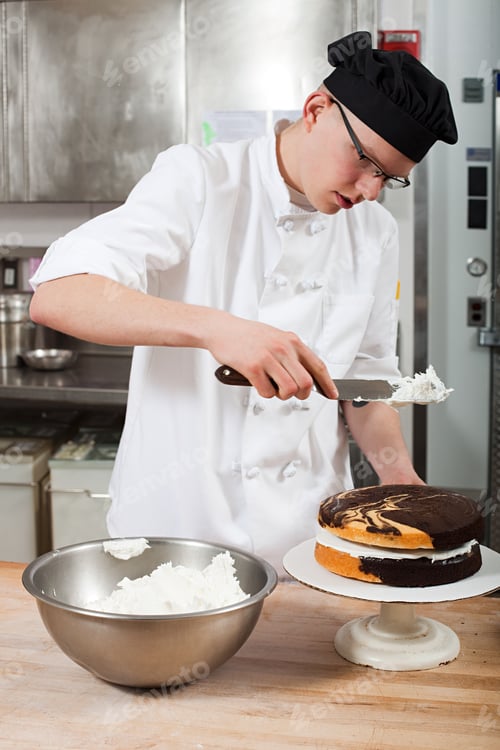 Preview: Male chef icing a cake in commercial kitchen