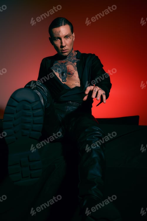 Preview: Stylish young man showing confident attitude with striking tattoos in a moody setting
