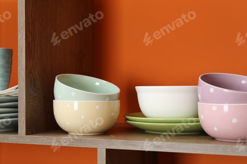 Preview: Different dishware on wooden shelf near orange wall indoors, closeup