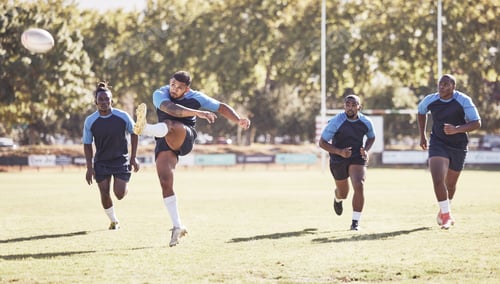 Preview: Mixed race rugby player attempting a dropkick during a rugby match outside on the field. Hispanic m