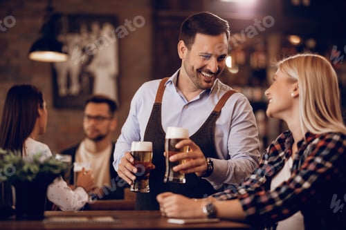 Preview: Happy waiter communicating with a guest while serving her beer in a pub.