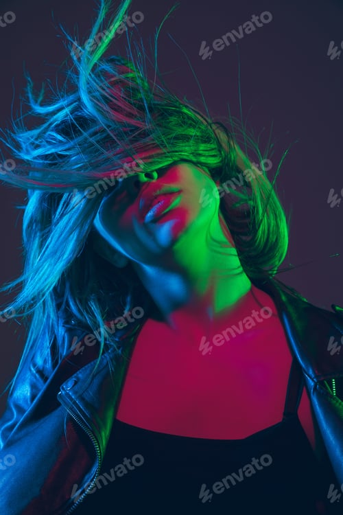 Preview: Beautiful woman's portrait with blowing hair on dark studio background in colorful neon light