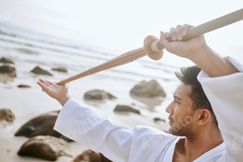 Preview: Shot of a young martial artist practising karate with a wooden katana on the beach
