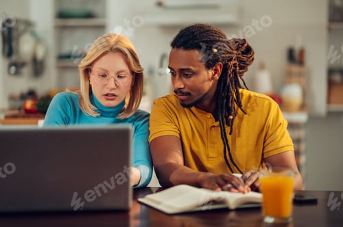 Preview: A serious multiracial couple is sitting at home with their laptop and doing calculations for bills.