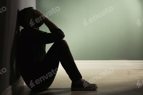Preview: Depressed young man sitting on floor in darkness