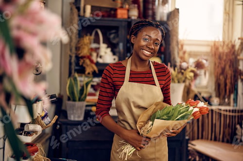 Preview: Happy African American florist holding bouquet of tulips and looking at camera.