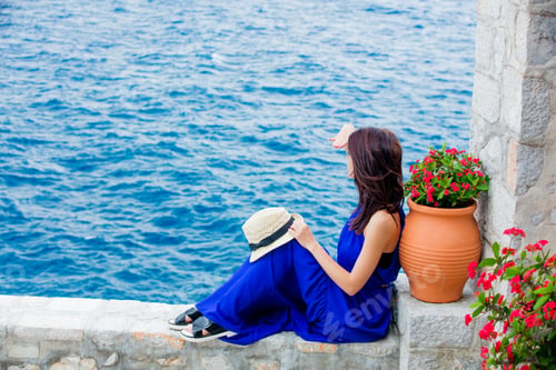 Preview: photo of beautiful young woman sitting near ot with flowers on the sea background
