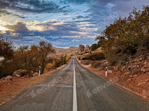 Preview: Empty open road with white dividing line through beautiful landscape during golden hour.