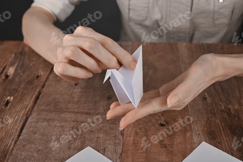 Preview: hands of an elderly woman fold origami paper. Creating an origami paper crane