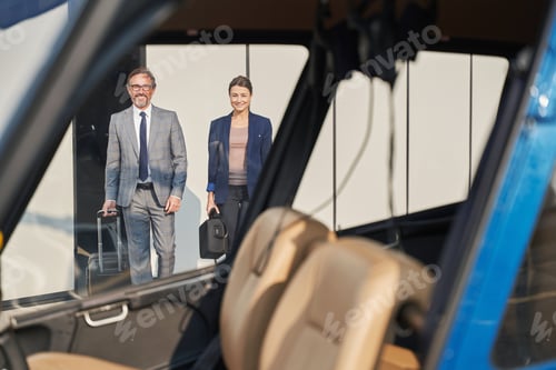 Preview: Two smiling businesspeople with baggage approaching helicopter