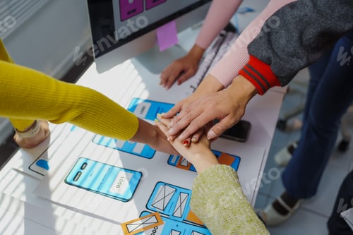 Preview: App developers joining hands over a table with app design sketches