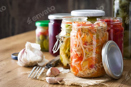 Preview: Preserved vegetables in glass jars with garlic cloves and fork on rustic wooden table