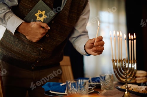 Preview: Close up man holding Hebrew bible while lighting the menorah.