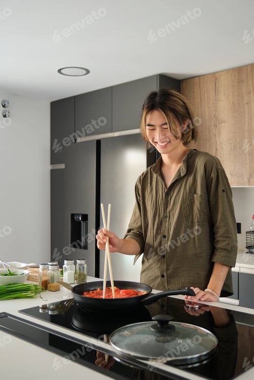 Preview: Asian young man cooking chinese or taiwanese tomato scrambled eggs at kitchen.