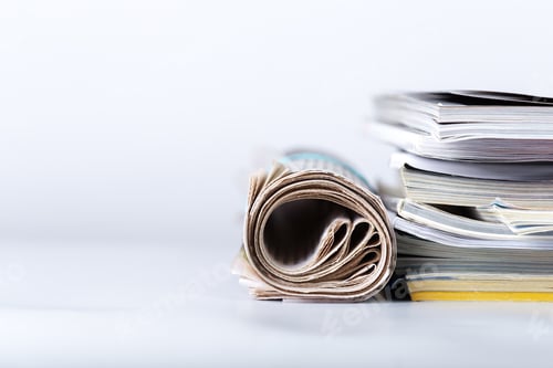Preview: Stack of magazines and rolled newspaper on white surface in indoor setting