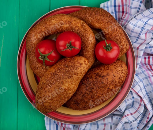 Preview: top view of soft and sesame patties on a bowl with fresh tomatoes on a cloth on a green wooden