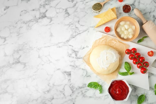Preview: Dough and ingredients for pizza on marble background, top view