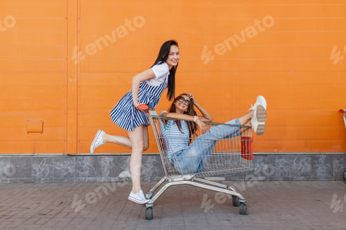 Preview: Two pretty slim dark-haired ladies,wearing casual outfit,have fun with a grocery cart near the