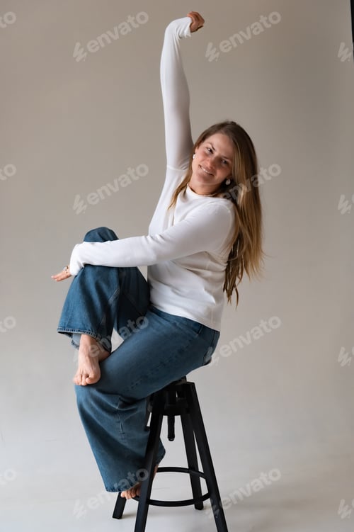 Preview: Pretty blonde woman with curly hair in jeans and a white sweater sitting on chair
