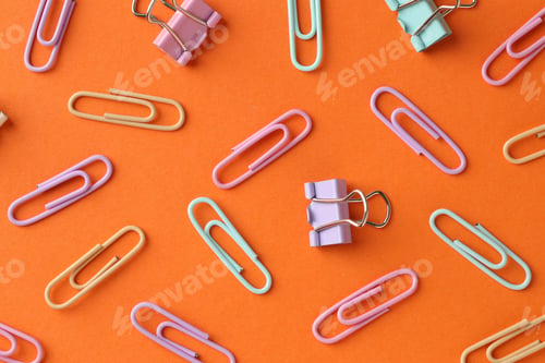 Preview: Colorful paper clips on orange background, flat lay