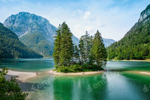Preview: Idyllic green alpine lake with tall trees on small island at Lake Raibl near Tarvisio in Italy.