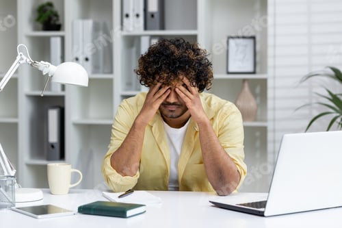 Preview: Stressed man sitting at desk in office overwhelmed by work with hands on face