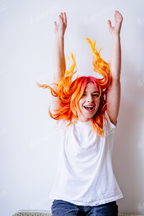 Preview: Joyful young woman with vibrant hair celebrating indoors