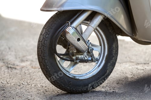 Preview: Close-up detail of new silver shiny motorbike scooter front wheel parked on blurred sunny background