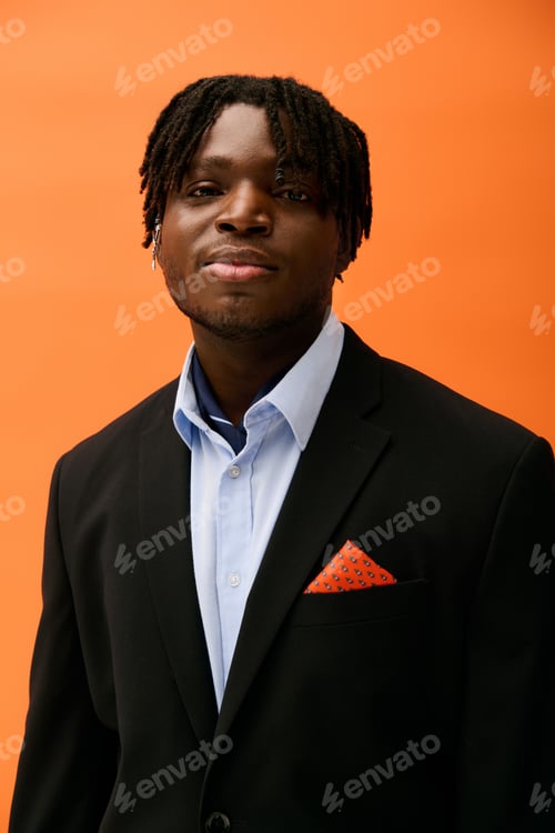 Preview: Stylish young man in a smart suit poses confidently against a vibrant orange background
