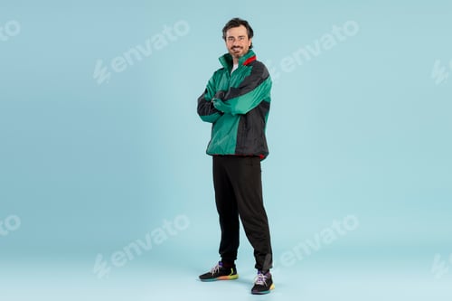 Preview: Confident sportsman smiling with crossed arms in studio shot