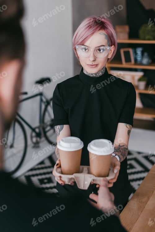 Preview: cropped shot of young tattooed woman giving paper cups to colleague