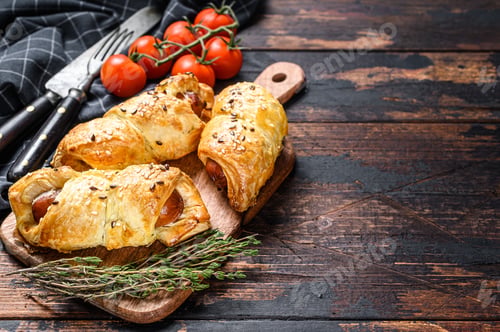 Preview: Cutting board with sausage rolls in the dough. Dark wooden background. Top view. Copy space
