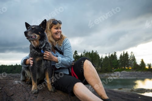 Preview: Senior woman sitting on rock hugging dog at coast of Maine, USA
