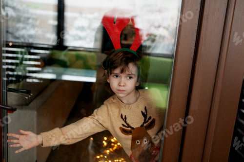 Preview: Child boy dressed in reindeer costume with antlers, standing near window, awaiting Christmas