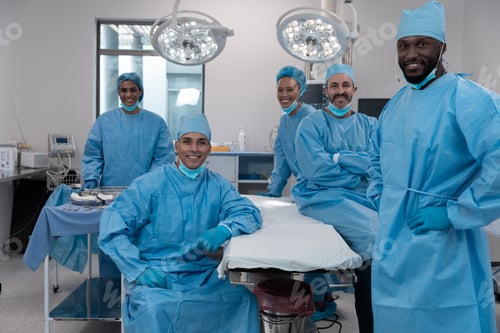 Preview: Smiling diverse surgeons with face masks and protective clothing in operating theatre