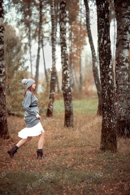 Preview: Woman in wool handmade gray knitted hat with a pompom and sweater enjoys nature walking autumn park