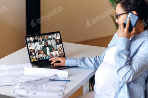 Preview: Successful busy mixed race pregnant woman is sitting near her work desk, having pleasant cellphone