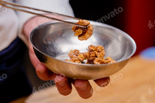Preview: close-up of a bowl of walnuts and the chef grabs them with tweezers to decorate the salad