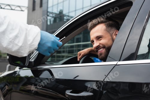 Preview: Smiling driver in car near medical worker with pcr test