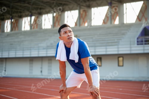 Preview: Asian man in blue t shirt is standing with hands on his knee and looking up in the sky.