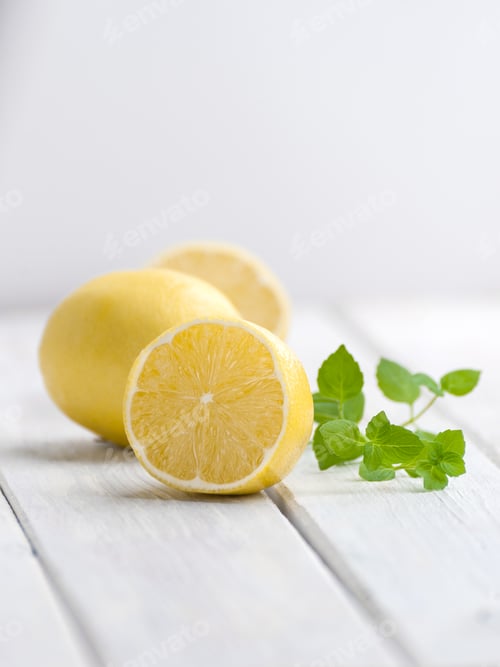 Preview: Half a ripe lemon and a mint branch on a white wooden table.