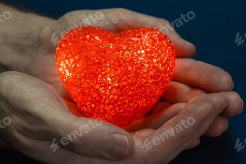 Preview: Red flaming heart in strong male hands on a blue background. Valentine's day concept. Close-up.
